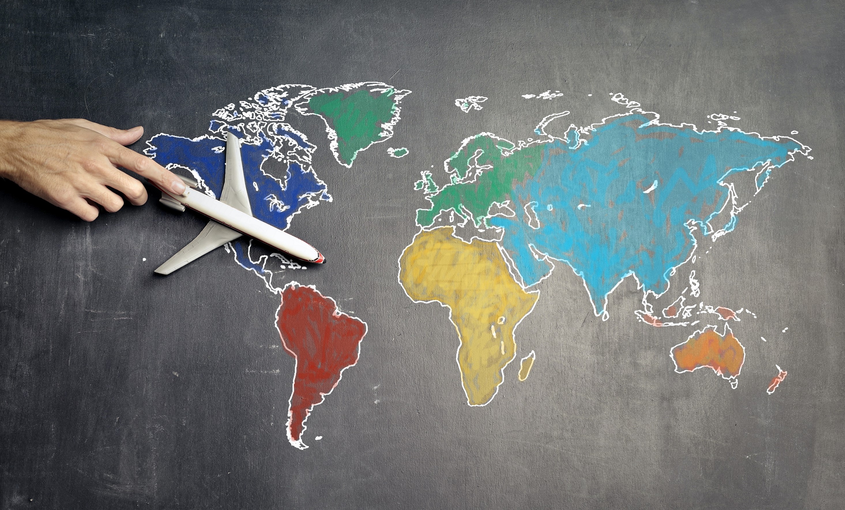 Hand pushing a toy airplane over a chalk world map